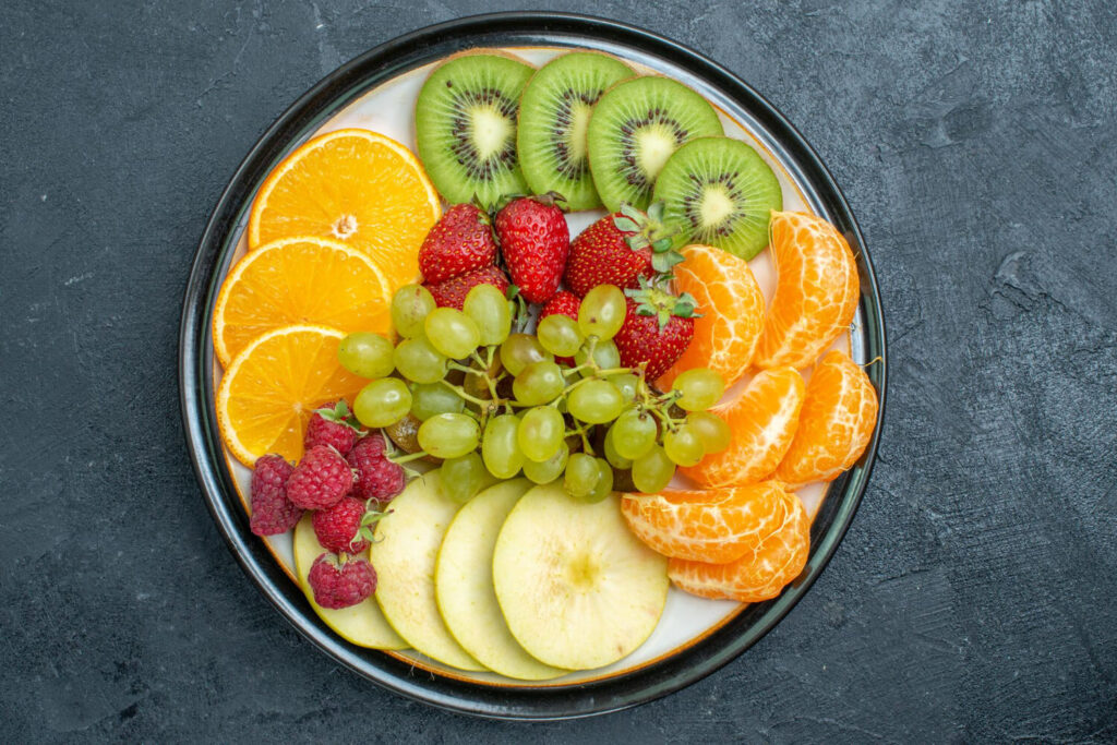 A top-view composition of a delicious assortment of fresh, sliced, and ripe fruits on a dark background, representing a healthy vitamin-rich diet.