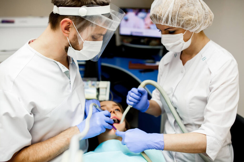 Dentists in full protective gear performing a deep cleaning procedure.