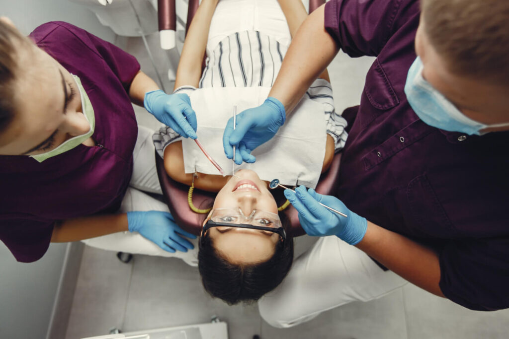 Overhead view of a beautiful girl about to undergo a deep dental cleaning, seated in a dentist's chair with dentists and cleaning tools by her side.