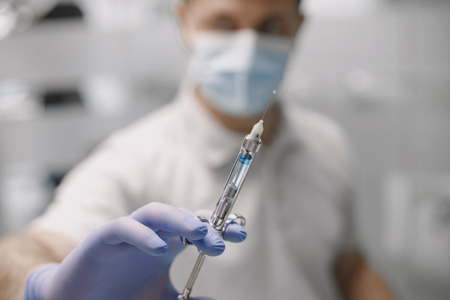 Close-up of a dentist's gloved hand holding a syringe, ready to administer pain relief injection for anesthesia.