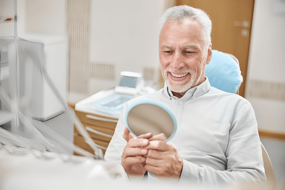 Elderly patient at a dental clinic, smiling while looking in the mirror, seated in a dental chair.